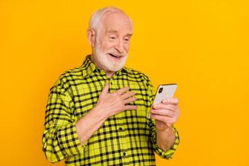 Photo of old man grandfather hand on chest happy smile grateful look browse cellphone isolated over yellow color background