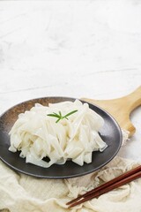 Grainy look Fresh Kwetiau as White Chinese noodles made from Rice in black plate. Popular in South East Asia on texture white background