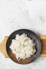 Wall Mural - Shiny Fresh Kwetiau as White Chinese noodles made from Rice. Popular in South East Asia in back plate with napkin and wood board on texture white background. Top view, Selective focus