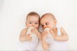 © Any Grant - two baby twins boy and girl with a bottle of milk on a white bed at home, baby food concept, place for text