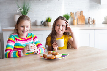 Portrait of two teenage beautiful smiling hipster girls in fashionable clothes. carefree children posing against the backdrop of the kitchen. Positive models have fun with sweets.