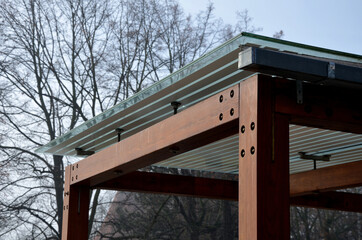 wooden structure of the bus stop, the shelter of the gazebo pergola. the roof and walls are lined with glass. the glass is anchored with stainless steel couplings. ceiling glass is white striped, sun 