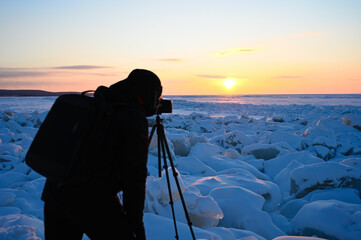 Photographer shoots a sunset among the snow-covered hummocks of Lake Baikal