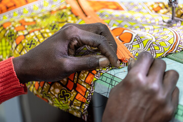 close up of hands of african tailor working, craftman making dress with traditional wax fabric from senegal