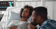Worried african husband sitting at sick wife bed in hospital