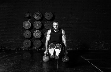 Young active sweaty fit strong muscular fit man with big muscles doing hardcore abs workout cross training with his legs up on the two kettlebells in the gym real people exercise