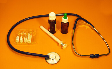 Stethoscope pills ampoules and tablets on orange background