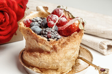 French dessert from bakery with golden spoon on white table with red roses on background. Focus on berries