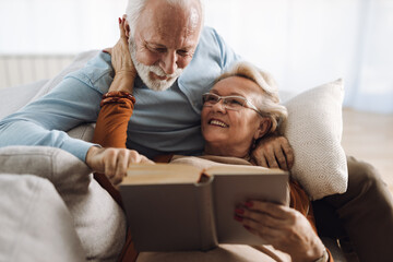 Wall Mural - Mature smiling couple having fun on the sofa while reading a book