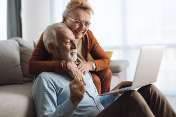 Wall Mural - Cheerful mature couple using laptop at home