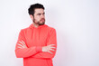 © Jihan - Displeased young Caucasian bearded man wearing pink hoodie against white wall with bad attitude, arms crossed looking sideways. Negative human emotion facial expression feelings.