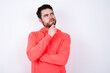 © Jihan - young Caucasian bearded man wearing pink hoodie against white wall with hand under chin and looking sideways with doubtful and skeptical expression, suspect and doubt.