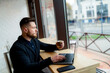 © Vadim - Young freelancer or businessman works on lap top and drinks coffee in a cafe. Big panoramic windows in front. Closeup.