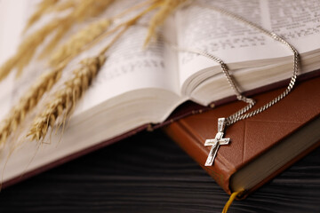 Silver necklace with crucifix cross on christian holy bible book on black wooden table. Asking blessings from God with the power of holiness