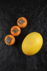 Ripe persimmon fruits and delicious melon on black surface