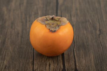 One ripe persimmon fruit placed on wooden surface