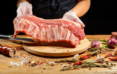 Wall Mural - The chef uses his hands to slice pork ribs with a knife on a wooden cutting table. Selective focus. The concept of the cooking process.