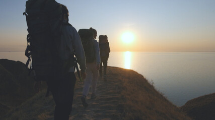 The tourists with backpacks walking on the mountain landscape near the sea