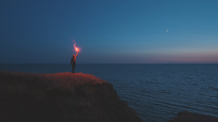 The man with a fire stick standing on the mountain top near the sea