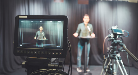 Young journalist in a television recording studio is talking into a microphone, blurry film cameras