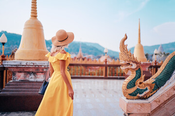 Wall Mural - Travel by Asia. Young woman in hat and yellow dress walking near the Chalong buddhist temple on Phuket Island in Thailand.