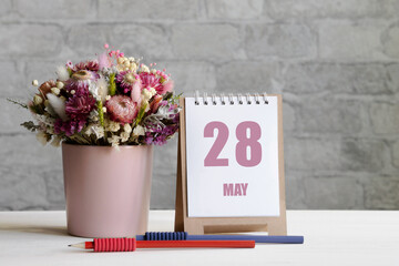 may 28. 28-th day of the month, calendar date.A delicate bouquet of flowers in a pink vase, two pencils and a calendar with a date for the day on a wooden surface