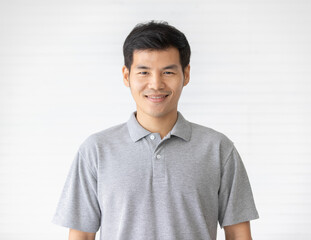 Portrait close up shot of handsome asian male model with short black hair wearing gray polo shirt stand smiling in front of white background