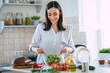 © My Ocean studio - Happy smiling cute woman is preparing a fresh healthy vegan salad with many vegetables in the kitchen at home and trying a new recipe