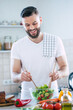 © My Ocean studio - Handsome happy bearded man is preparing wonderful fresh vegan salad in the kitchen at home
