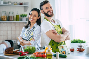 Wall Mural - Excited smiling young couple in love making a super healthy vegan salad with many vegetables in the kitchen and having fun