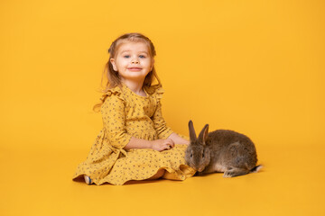 Wall Mural - funny cute child girl in yellow dress with rabbit sitting on yellow background