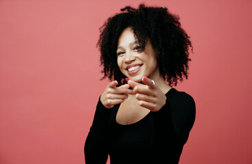 Wall Mural - shows a finger gesture to the camera and smiles, a young woman of Afro appearance. photo in a photo studio on a red background.