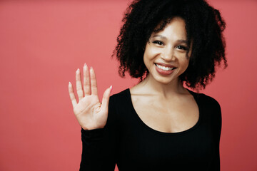 Wall Mural - shows a greeting gesture, a young cheerful beautiful woman with black curly hair. he smiles and shows white teeth. afro appearance model. photo on a scarlet background