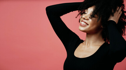 Wall Mural - joy dances her hands near her hair and looks into the camera portrait of a young Afro-ethno woman. A model in a photo studio poses on a scarlet background.