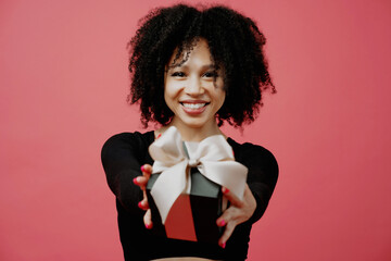 in the hands of a black box with a bow, the gift shows holding it. young woman of Afro appearance, curly lush hair. She is dressed in a black comfortable jacket. He looks at the camera and smiles.