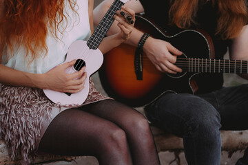 Redhead guy and girl playing acoustic guitar and ukulele. Outdoor