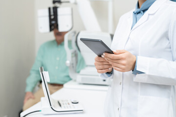 Poster - Hands of young female ophthalmologist in whitecoat using tablet against patient