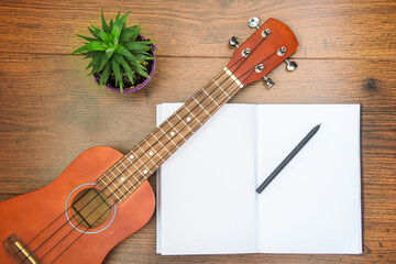 Ukulele four-string guitar on wooden table with a notebook and pen. Concept of learning to play musical instrument, self-education.