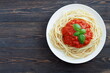 © Photo cook - Italian pasta, spaghetti with tomato sauce and basil on a white plate on a dark wooden background with copy space for your text