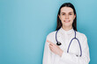 © Yura Yarema - Smiling happy doctor pointing with finger on copy space, wear white lab coat stethoscope, isolated on blue studio background. Covid-19, preventing virus, healthcare workers and vaccination concept