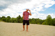 © YAROSLOVEPHOTOVIDEO - A young man in a bright multicolored shirt and cap stands on the sand near the forest