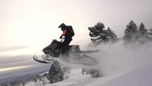 SLOW MO: Video Footage Of Jumping Snowmobilers At Sunset. The Snowmobile Flies Through The Air And Creates Large And Beautiful Swirls Of Snow. ProRes 422. HD 500fps