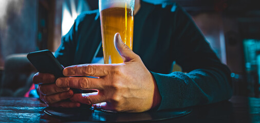 Wall Mural - close up of man hand hold smartphone, drinking beer and reading message at bar or pub