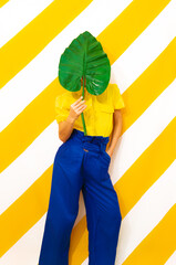 Model holding palm leaf and wearing vintage look on trendy striped yellow background. Minimal fashion spring summer concept. Stylish colours combination.