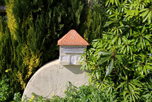 Stone Letterbox In The Shape Of A House Surrounded By Green Plants 