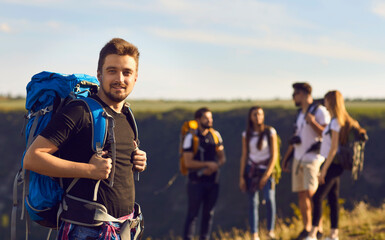 Wall Mural - a young tourist man with a backpack looks at the camera on a hike against the background of friends 