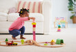 cute african american toddler baby girl playing wooden toys, stacking the tower blocks on the carpet at home
