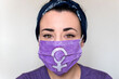 © AliciaFdez - Retrato en primer plano de una mujer joven con una mascarilla quirúrgica morada para el coronavirus con el símbolo de la mujer. Concepto de Día Internacional de la Mujer en tiempos de pandemia. 8M