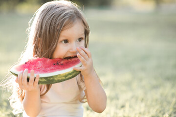 Cute baby girl 3-4 year old eating tasty watermelon over green nature background close up. Healthy lifestyle. Childhood. Summer time.