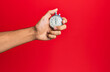 © Krakenimages.com - Hand of young hispanic man using stopwatch over isolated red background.